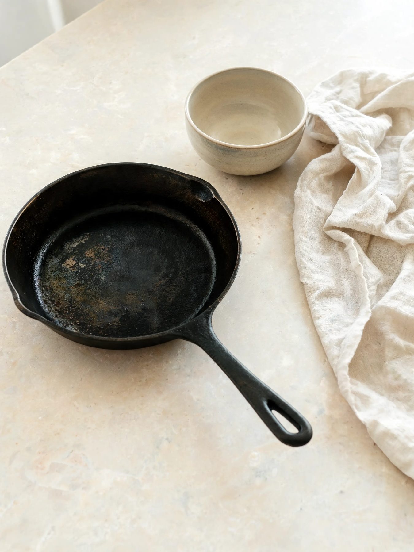 Seasoned skillet and glazed stoneware bowl on a limestone counter
